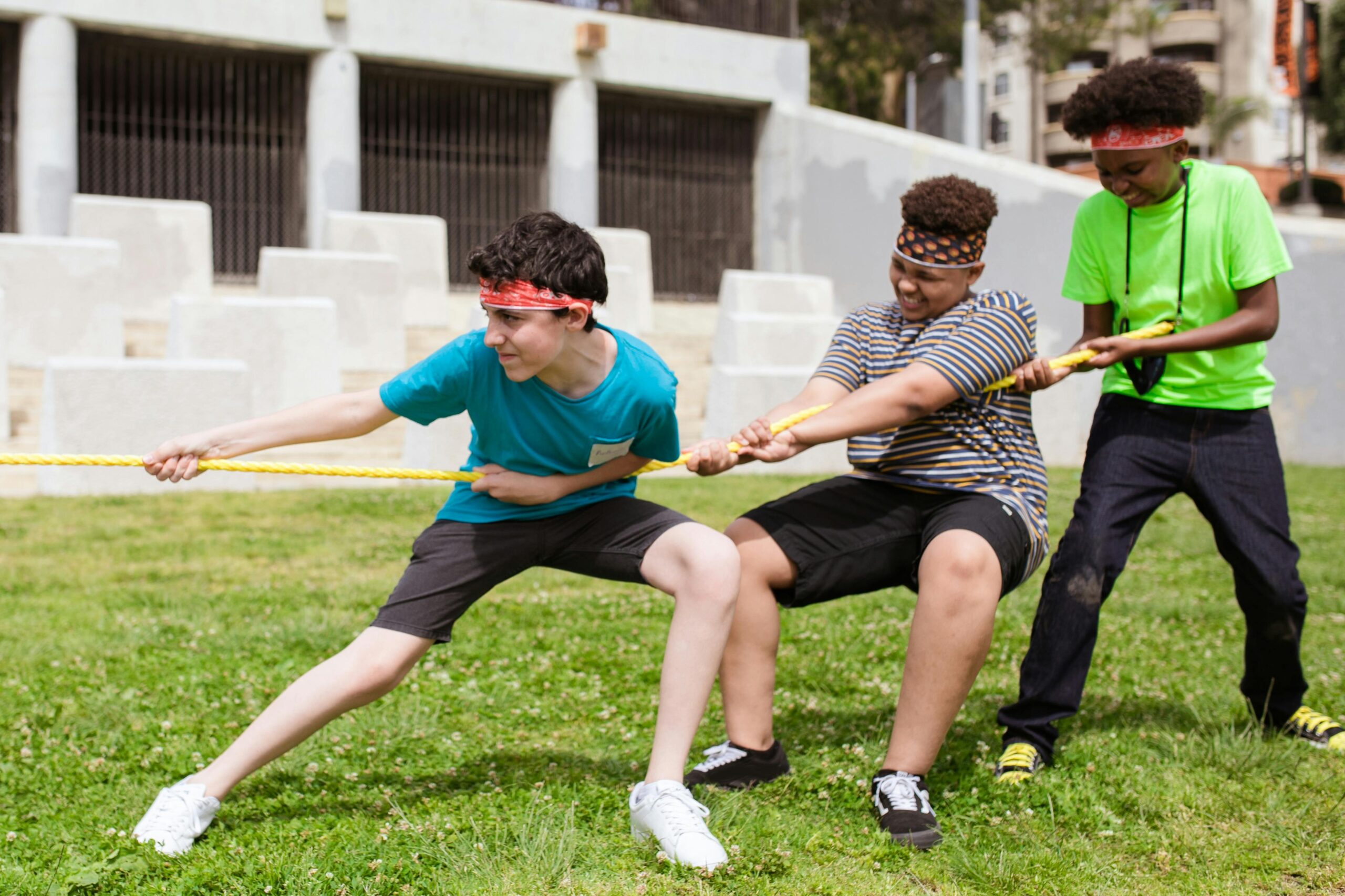 Group of boys playing tug of war on green grass during summer camp, enjoying outdoor fun and teamwork.