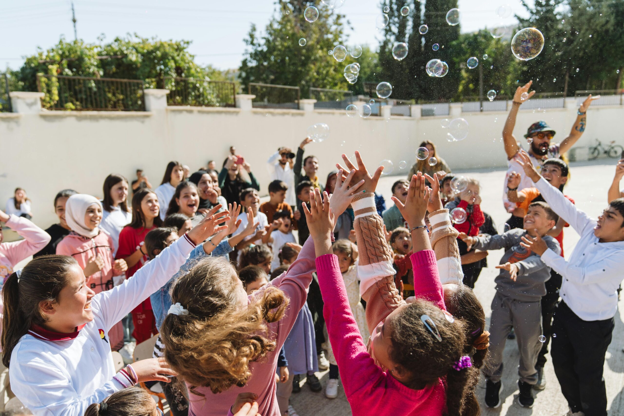 Joyful children playing with bubbles in a sunny outdoor setting, surrounded by adults.