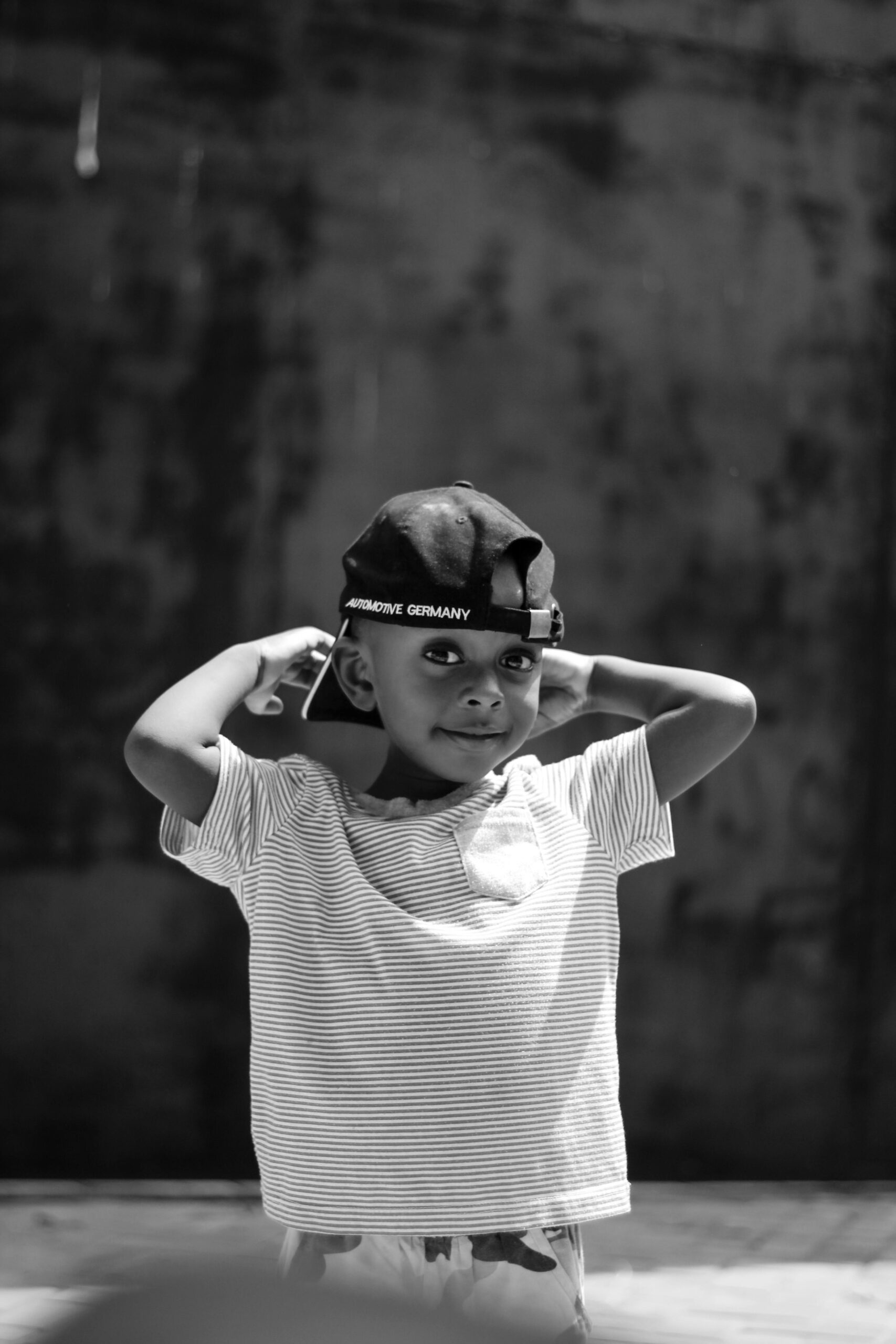 A cute child with a cap poses playfully in a black and white portrait.